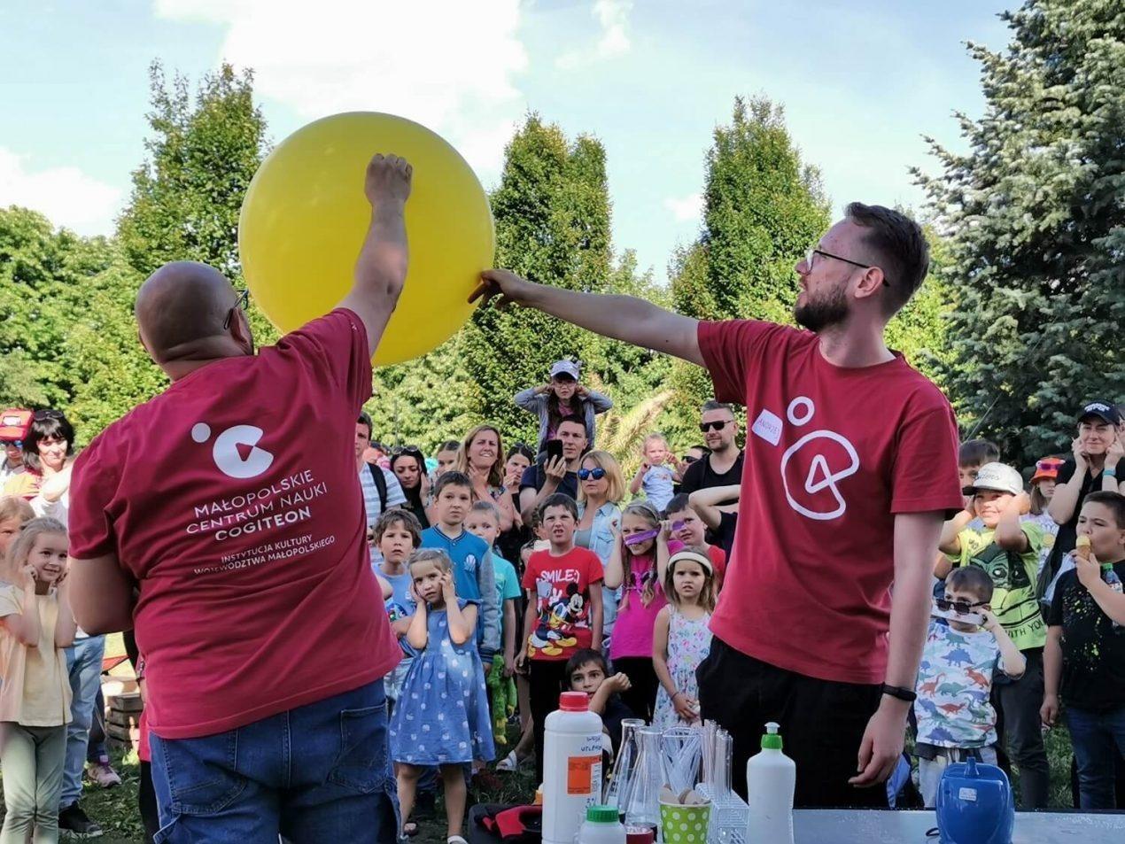 Zdjęcie z pokazu. Dwóch edukatorów stoi w plenerze przed publicznością demonstrując wielki balon.