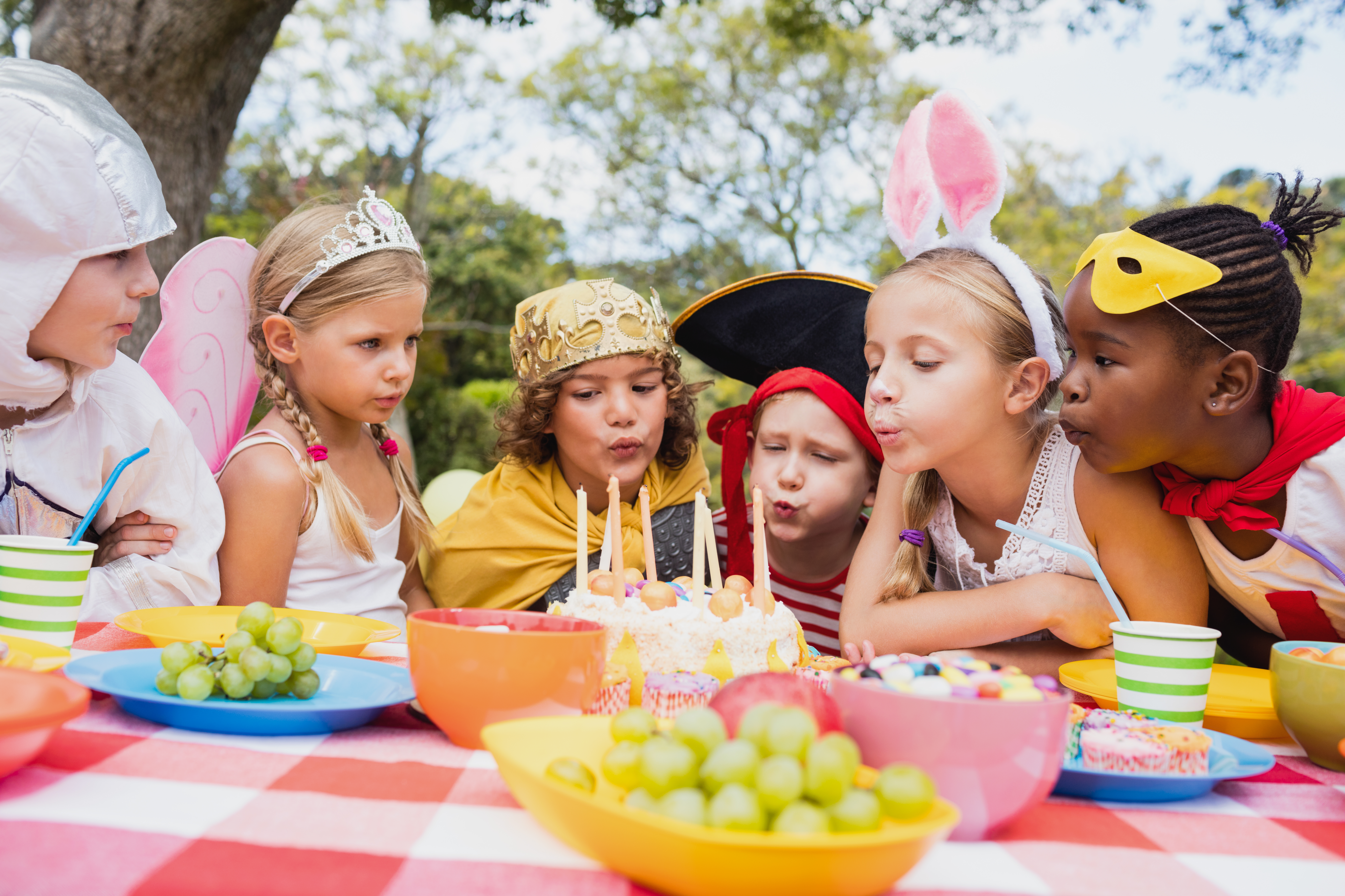 Zdjęcie przedstawiające 6 dzieci przy zastawionym w plenerze stole. Widoczne owoce oraz tort urodzinowy.