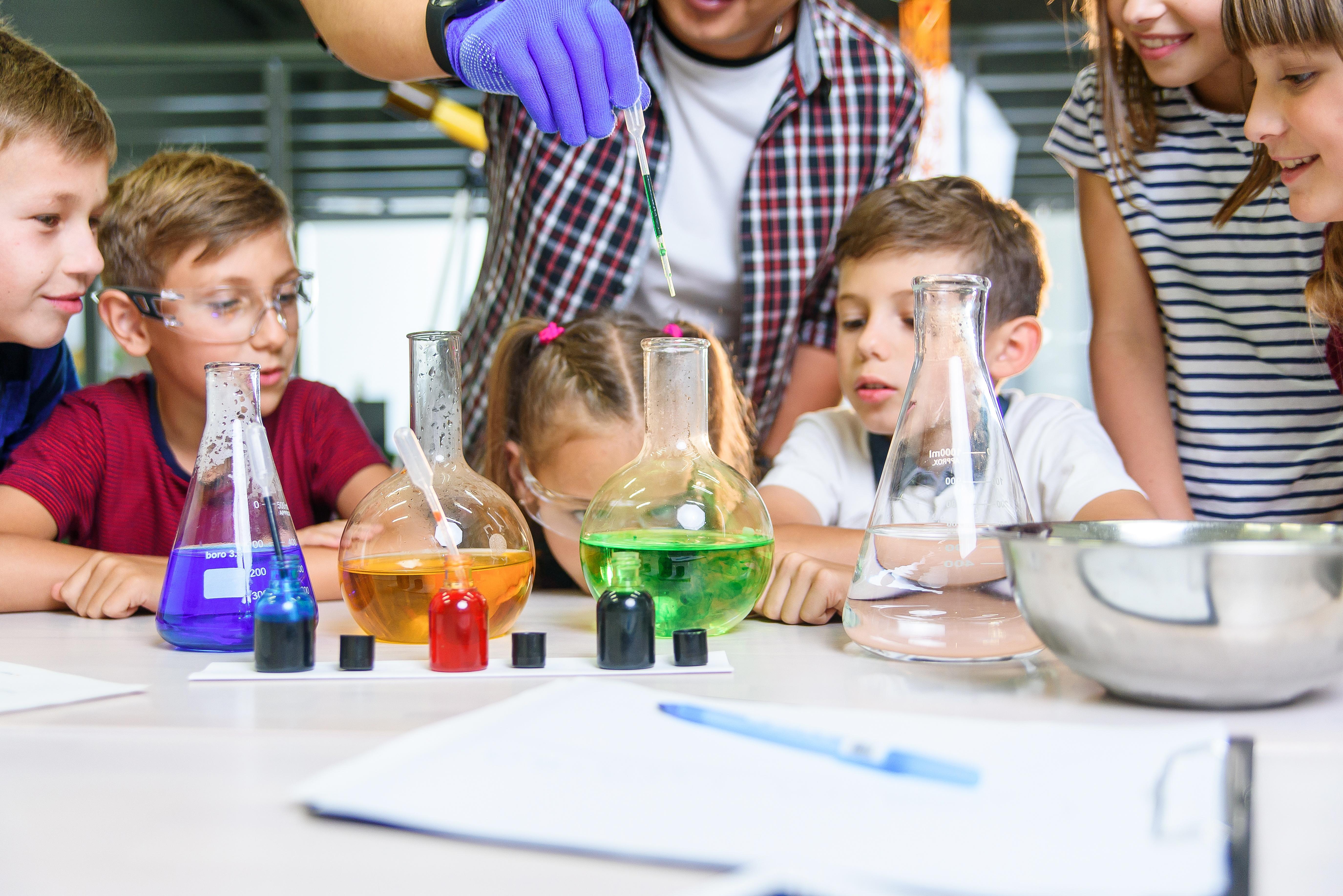 Dzieci w laboratorium spoglądają na kolorowe naczynia podczas przeprowadzania doświadczenia chemicznego.