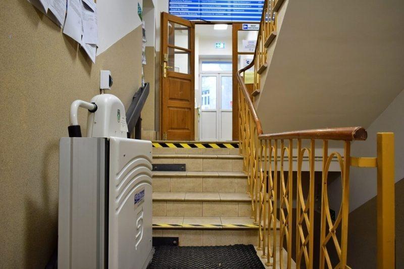 Schody na wysoki parter, gdzie znajdują się pomieszczenia biurowe. Za drzwiami, po lewej stronie znajduje się portiernia. Zdjęcie schodów prowadzących na wysoki parter. Widoczny podnośnik.