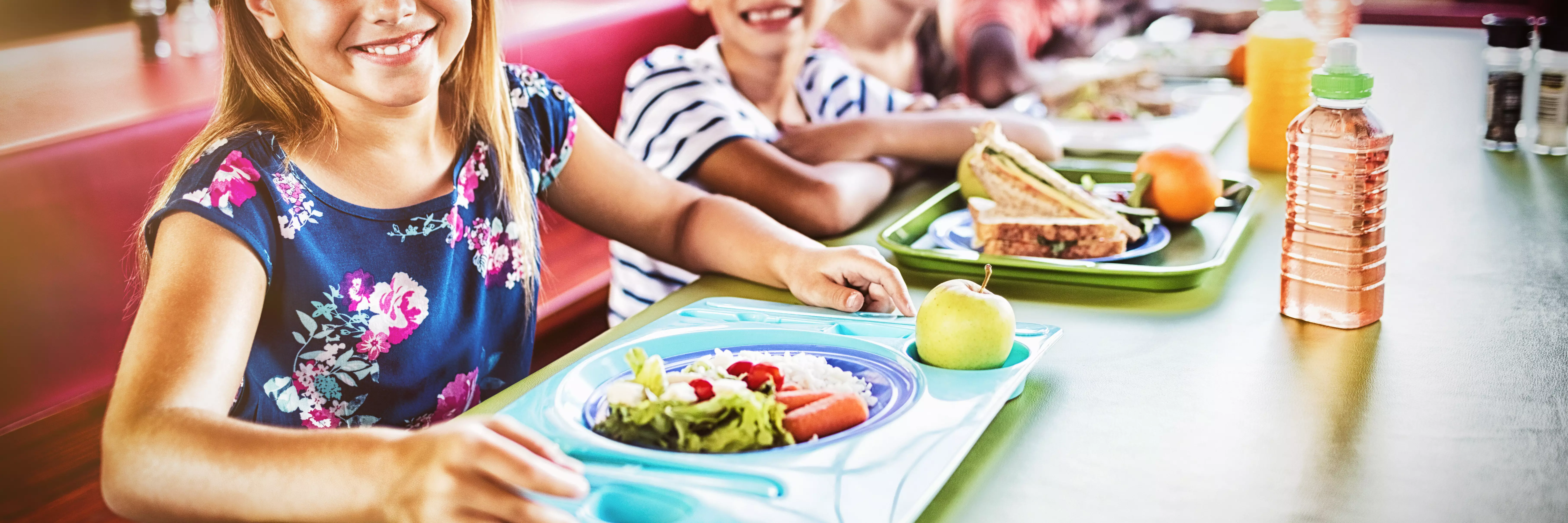 Uśmiechnięte dzieci siedzą przed tacami z jedzeniem.